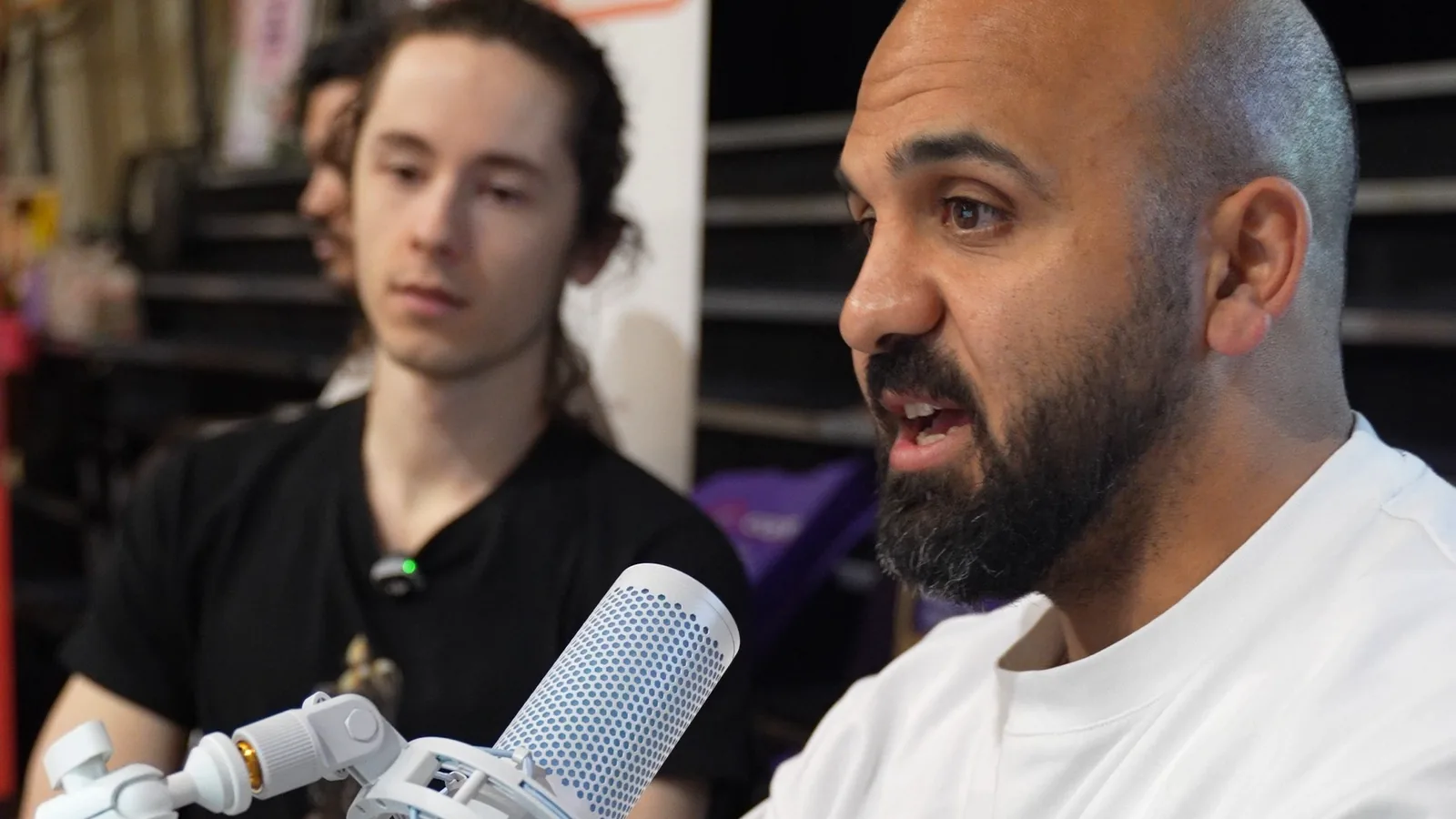 Hamid speaking into a microphone at the CH3CKPOINT expo stand, with team member Sebastian beside him